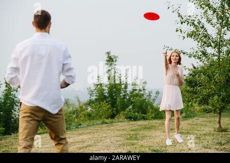 Mann und Frau spielen Frisbee in einem Park neben einem Fluss und einem Waldrücken Stockfoto