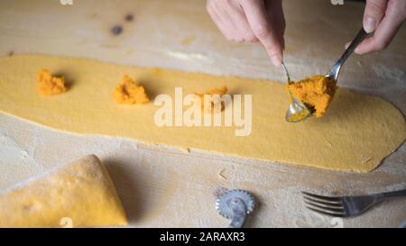 Closeup-Prozess, bei dem Ravioli vegane hausgemachte Pasta hergestellt werden. Hausfrau Koch die Füllung des "Tortelli di zucca" auf das Gebäck legen und mit einem sp messen Stockfoto