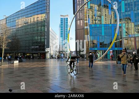 Deliveroo Radfahrer auf Fahrrad und Skulptur außerhalb der Cardiff Central Library und John Lewis in der Einkaufsgegend des Stadtzentrums von Cardiff Wales UK KATHY DEWITT Stockfoto