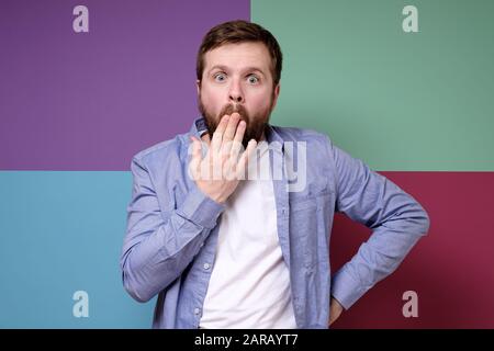 Der kaukasische bärtige Mann ist überrascht und schockiert, er schloss den Mund mit der Hand und blickt mit großen Augen in die Kamera. Stockfoto