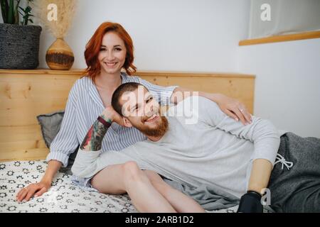 Glückliches Ehepaar, das zu Hause auf ein Doppelbett kühle. Posieren für ein Foto. Stockfoto