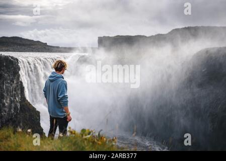 Wanderer, der am Rande des Dettifoss Wasserfalls in Island steht Stockfoto