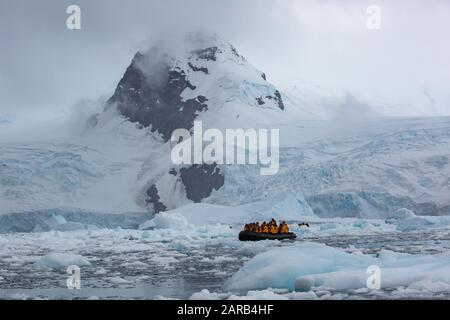 Touristen auf einem Schlauchboot aus dem Gummi-Tierkreis, der durch Eisschollen in den kalten Gewässern der Antarktis segelt Stockfoto