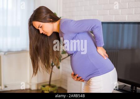 Schwangere Frau, die Schmerzen im Rücken hat, ist besorgt. Stockfoto