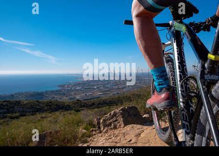 Mountainbiker auf einem Hügel mit Blick auf die Mittelmeerküste, das Dorf El Campello, Costa Blanca, Provinz Alicante, Spanien Stockfoto