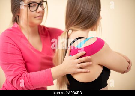 Junge weibliche Patienten mit kinesio Tape auf ihrer Schulter Training mit einem professionellen Physiotherapeuten. Kinesiologie, Physikalische Therapie, Sanierung Stockfoto