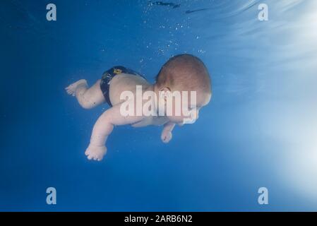 Der kleine Junge lernt, unter Wasser zu schwimmen. Baby schwimmend unter Wasser im Pool auf blauem Wasserhintergrund. Gesunde Familie und Kinder Wasser sp