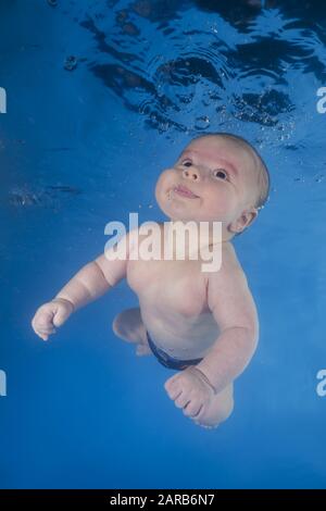 Der kleine Junge lernt, unter Wasser zu schwimmen. Baby schwimmend unter Wasser im Pool auf blauem Wasserhintergrund. Gesunde Familie und Kinder Wasser sp
