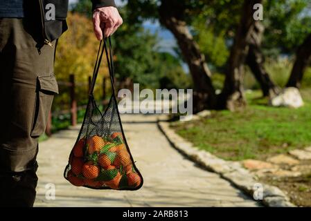 Mann mit wiederverwendbarer Mesh-Einkaufstasche mit frisch gepickten Orangen. Null-Abfall-Konzept. Sonniger Tag Stockfoto