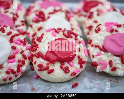 Thumbprint-Plätzchen, die zum Valentinstag auf einem rustikalen silberfarbenen Tablett mit Frost verziert sind, und rot, weiß und pink gesprinklt. Stockfoto