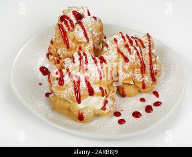 Profiteroles mit Käsecreme oder Eiscreme auf einem Teller, der mit Puderzucker verziert ist. Stockfoto