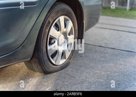Flacher Hinterreifen auf grünem Auto an der Einfahrt des Parkhauses in der Nähe Stockfoto