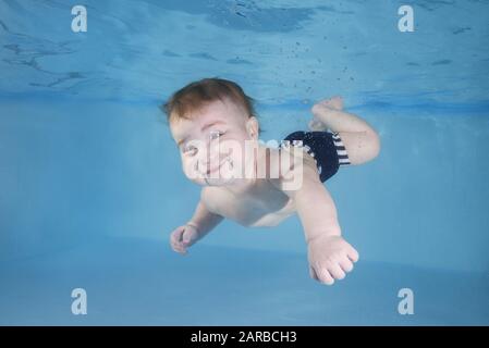 Kleiner Baby-Junge lernt unter Wasser zu schwimmen. Baby schwimmend unter Wasser im Pool. Gesunder Familienleben und Wassersport für Kinder. Kind d