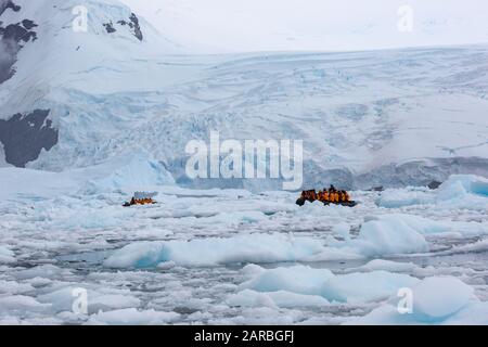 Touristen auf einem Schlauchboot aus dem Gummi-Tierkreis, der durch Eisschollen in den kalten Gewässern der Antarktis segelt Stockfoto