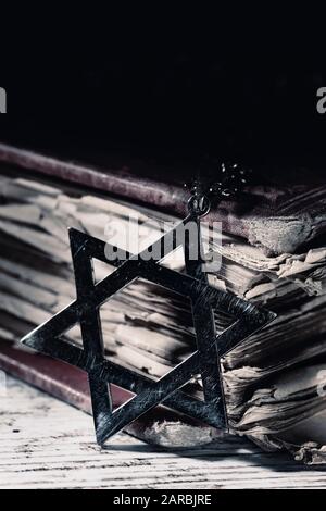Nahaufnahme eines alten und rostigen Pendants in Form des Davidstars neben einem alten Buch, auf einer rustikalen Holzoberfläche, mit einem dramatischen Licht Stockfoto