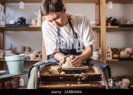 Potter, der an einem Potter-Rad arbeitet und eine Vase macht. Junge Frau, die den Ton mit ihren Händen formt und in einer Werkstatt Kanne schafft. Stockfoto