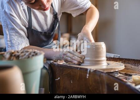 Potter, der an einem Potter-Rad arbeitet und eine Vase macht. Junge Frau, die den Ton mit ihren Händen formt und in einer Werkstatt Kanne schafft. Stockfoto