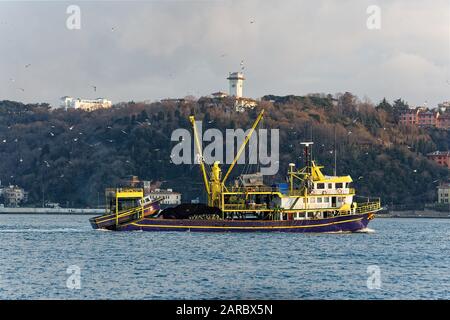 Kommerzielles Fischerboot vom Typ Trawler, das durch die Bosporus-Straße in Istanbul segelt. Ein großes Rettungsboot hing auf dem Rücken und Möwen umflogen. Stockfoto