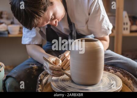 Frau Töpfer, die an einem Potter-Rad arbeitet, das eine Vase macht. Meister, der den Ton mit ihren Händen formt und in einer Werkstatt Kanne schafft. Nahaufnahme Stockfoto