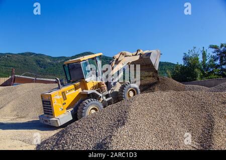 Traktorlader lädt Schutt an einem sonnigen Tag. Trümmerhaufen. Ein Traktor transportiert den zerkleinerten Stein von einem Haufen zum anderen Stockfoto