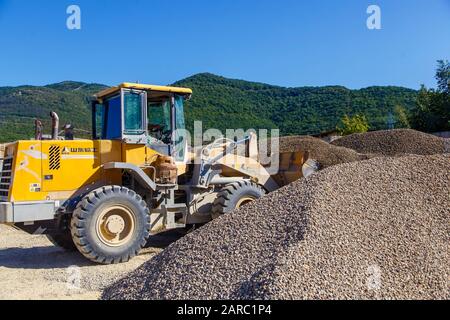 Traktorlader lädt Schutt an einem sonnigen Tag. Trümmerhaufen. Ein Traktor transportiert den zerkleinerten Stein von einem Haufen zum anderen Stockfoto