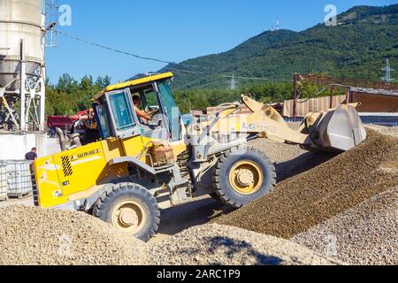 Traktorlader lädt Schutt an einem sonnigen Tag. Trümmerhaufen. Im Hintergrund das Geschäft für die Betonherstellung. Die Ausrüstung für den Stockfoto