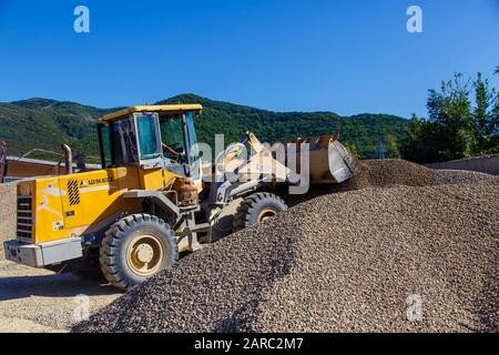 Traktorlader lädt Schutt an einem sonnigen Tag. Trümmerhaufen. Ein Traktor transportiert den zerkleinerten Stein von einem Haufen zum anderen Stockfoto