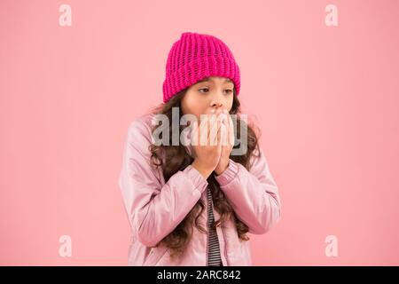 Keine Grippe in diesem Winter. In der kalten Jahreszeit warme Kleidung tragen. Winterferienaktivität. Kleine pinkfarbene Wand. Modischer Stil für Kinder. Strickmütze und Puffer-Mantel. Kleines Mädchen fangen Husten. Es ist so kalt. Stockfoto