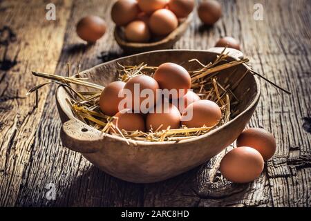 Frische rohe Eier in Strohhalm und Holzschale auf rustikalem Holztisch Stockfoto