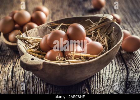 Frische rohe Eier in Strohhalm und Holzschale auf rustikalem Holztisch Stockfoto