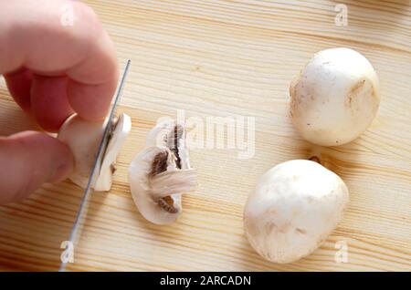 Die Hand eines Kochers hält ein Messer und schneidet Pilze auf einem Holzbrett. Stockfoto