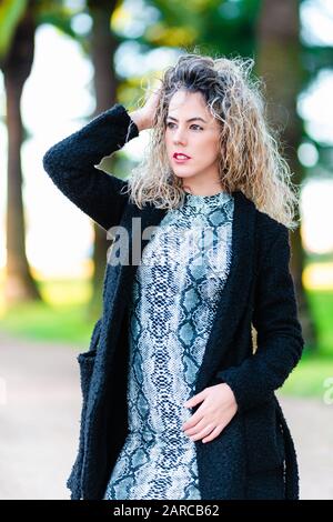 Junge Frau model mit lockig blonden Haaren, die im Park posieren Stockfoto