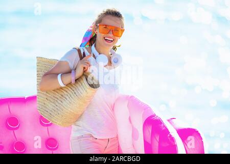 Porträt einer lächelnden trendigen Frau in weißem T-Shirt und pinkfarbenen Shorts mit Strandabschnitt auf der aufblasbaren Matratze. Stockfoto