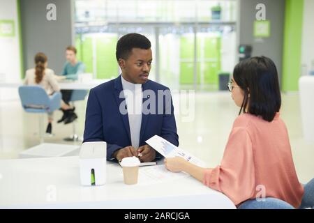 Portrait junger afrikanischer Geschäftsmann, der während der Mittagspause im Büro mit einer weiblichen Kollegin über Datendokumente spricht Stockfoto