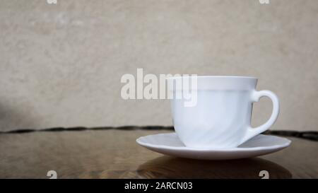 Heißer aromatischer Kaffee mit Milch. Frisch zubereitetes Getränk wird in einer modernen Tasse auf einem leichten Korbtisch serviert. Stockfoto