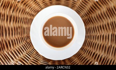 Kaffeetasse auf dem Korbhintergrund, Draufsicht. Heißer aromatischer Kaffee mit Milch. Frisch zubereitetes Getränk wird in einer modernen Tasse auf einem leichten Korbtisch serviert Stockfoto
