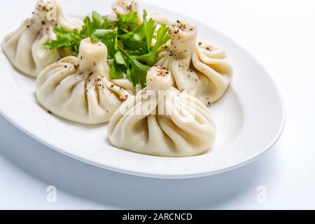 Georgisches Khinkali und ein Haufen Petersilie auf einem Teller. Die Platte befindet sich auf einem weißen Hintergrund Stockfoto