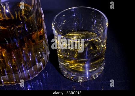 Dekanter und Glas mit Whisky auf schwarzem Hintergrund. Dekanter und Glas werden auf einem Glastisch gespiegelt. Stockfoto