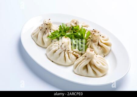 Georgisches Khinkali und ein Haufen Petersilie auf einem Teller. Die Platte befindet sich auf einem weißen Hintergrund Stockfoto