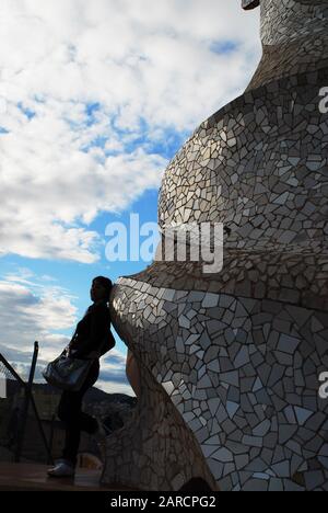 Eine Frau stellt sich gegen die symbolträchtigen dekorativen Kamine auf dem Dach der Casa Mila alias La Pedrera, dem berühmten Gebäude des katalanischen Architekten Antonio Gaudi. Stockfoto