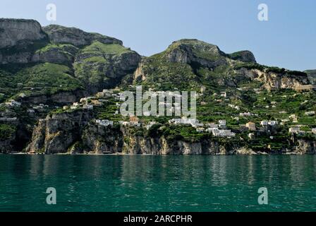 Steile terrassenförmige Weinberge und weiße Häuser an den Klippen der Amalfiküste sind vom Wasser in Kampanien, Italien, zu sehen. Stockfoto