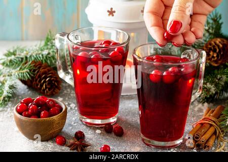 Weihnachtsgetränke. Weibliche Handhaltung von heißem Wintergetränk mit Preiselbeeren und Zimt auf einem hellen Steintisch. Stockfoto