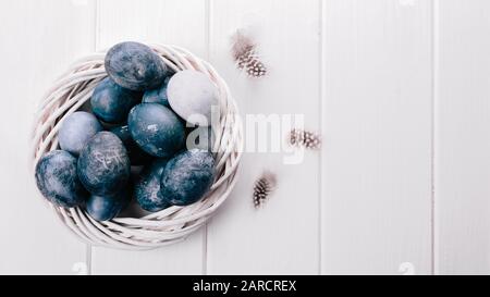 Gruppe hellblauer Eier in ihrem Gelege auf weißem Holzhintergrund. Fröhliche Osterdekoration. Klassische blaue Farbe des Jahres 2020 Stockfoto