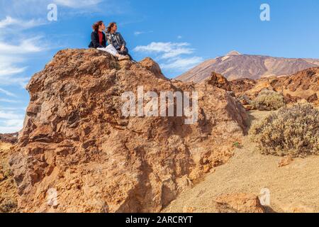 Zwei junge Frauen sitzen auf Felsen und blicken auf den Berg teide tenera-spanien im Nationalpark Stockfoto