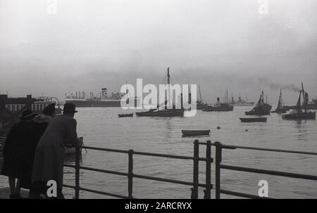 40er Jahre, historisch, Vater, Mutter und Tochter in Gravesend, Kent, England, Großbritannien, mit Blick auf den Hafen und die vermoorten Boote einschließlich eines Dampfschiffs. Bis zum Bau der Tilbury-Docks im Jahr 1886 war Gravesend der erste Hafen der Themse. Stockfoto