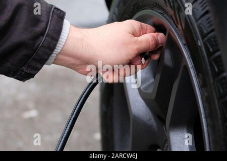 Mann prüft Druck in Autoreifen. Das Ventil des Autoreifens von Hand anbringen. Nahaufnahme. Stockfoto