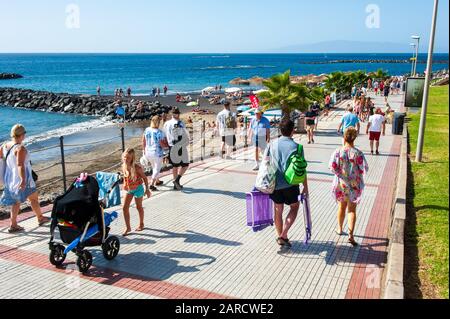 KANARENINSEL TENERA, SPANIEN - 27 DEC, 2019: Touristen, die auf der Strandpromenade entlang der Playa El Duque spazieren. Es ist einer der beliebtesten Strände auf der Insel. Stockfoto