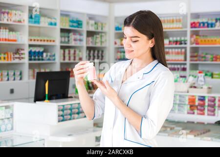 Attraktive Apothekerin mit sanften Händen, die einen kleinen Krug mit Medikamenten oder Vitaminen in einer Apotheke hält Stockfoto