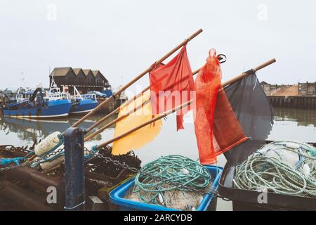 Boje Flaggenmacher an Stöcken über Seil und angeln nächste Körbe im Whitstable Hafen. Fischerhütten und Fischerboote sind im Hintergrund zu sehen Stockfoto