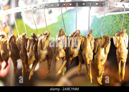 Lebensmittelgeschäft in asien. Kadaver von seltsamen gelben Hühnern, die an einer Vitrine an Metallhaken hängen. Stockfoto